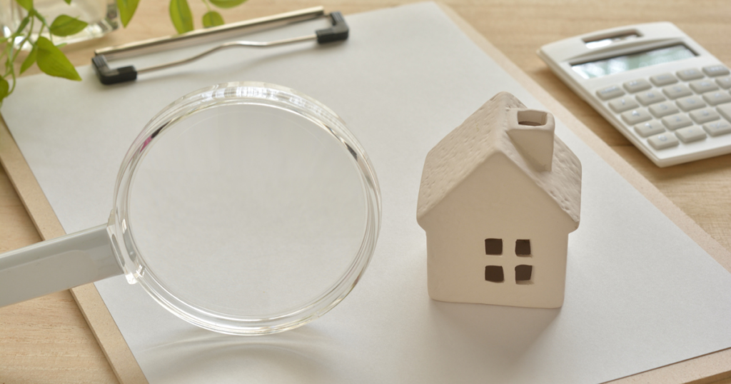 house figurine on a clipboard with a magnifying glass and calculator